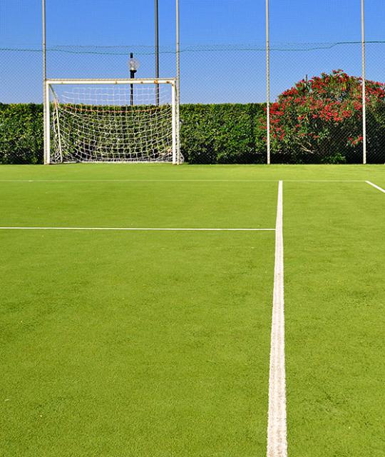 Campo da calcio vuoto, erba verde brillante, cielo azzurro, atmosfera serena e tranquilla.