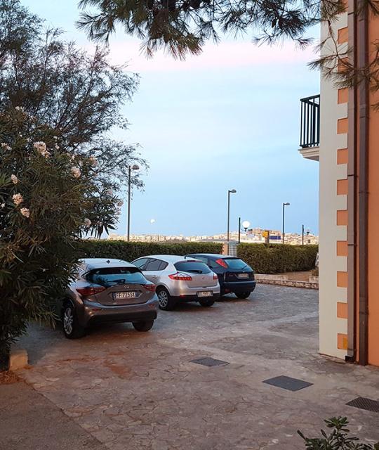 Auto parcheggiate al tramonto, cielo sereno e atmosfera tranquilla tra alberi e case.