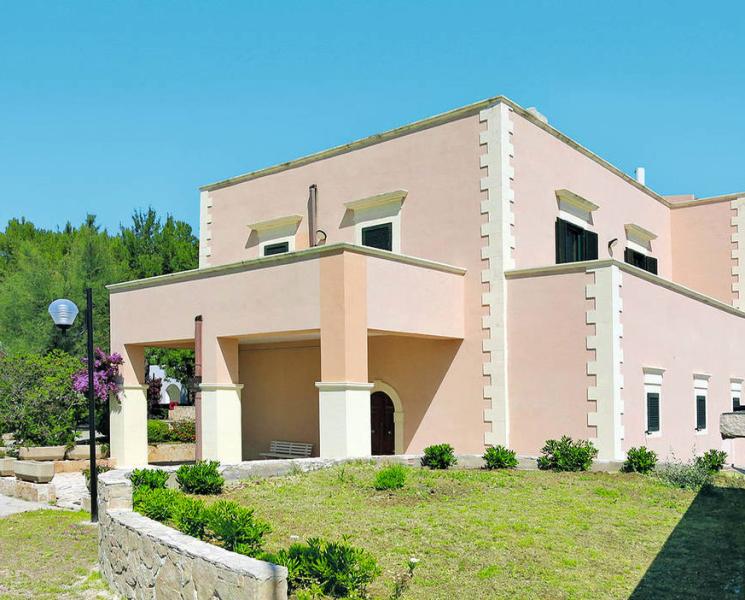 Edificio rosa con dettagli bianchi, immerso nel verde, evoca calma e serenità.