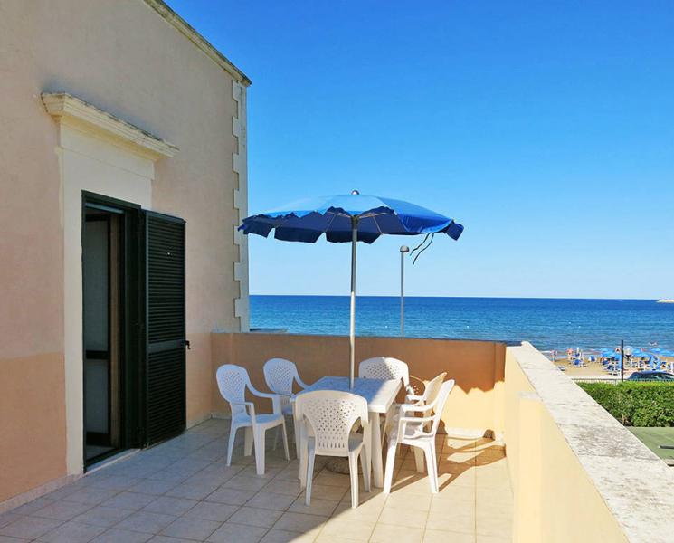 Terrazza assolata con tavolo, sedie e vista mare. Atmosfera rilassante e vacanziera.