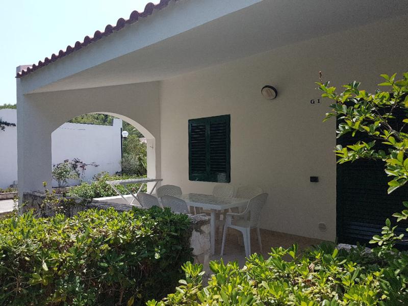 Veranda soleggiata con sedie bianche, circondata da verde, atmosfera tranquilla e rilassante.