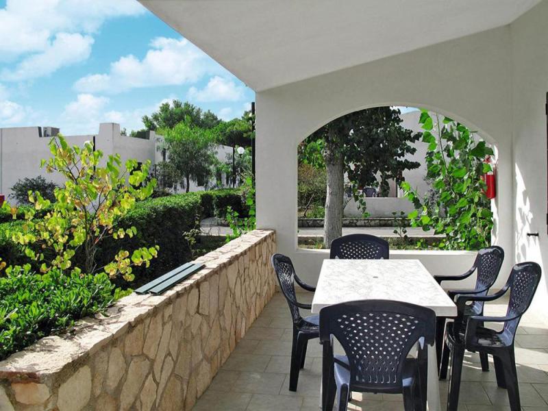 Terrazza luminosa con tavolo, sedie nere e vista su giardino verde e cielo azzurro.