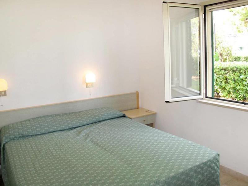 Camera luminosa con letto matrimoniale, finestra aperta su giardino verde, atmosfera serena.
