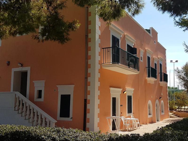 Edificio arancione con balconi, immerso nel verde, evoca tranquillità e calore mediterraneo.