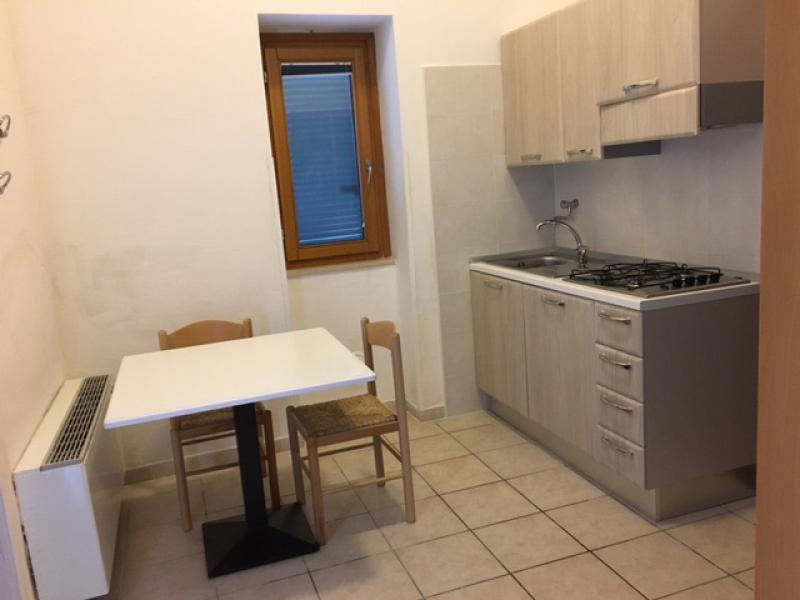 Terrazza soleggiata con vista mare, sedie bianche e ombrellone blu, atmosfera rilassante.