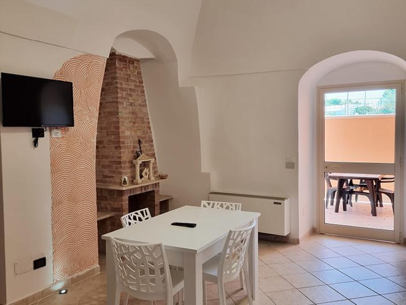Interno luminoso con tavolo bianco, camino in mattoni e atmosfera accogliente.
