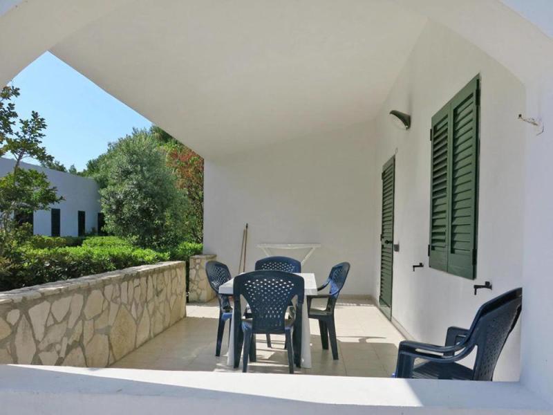 Veranda soleggiata con sedie di plastica, immersa nel verde, atmosfera rilassante e tranquilla.